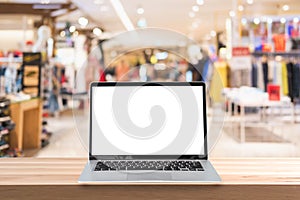 Empty screen laptop on a wooden table with abstract blurred background of interior clothing store