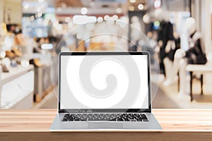 Empty screen laptop on a wooden table with abstract blurred background of interior clothing store