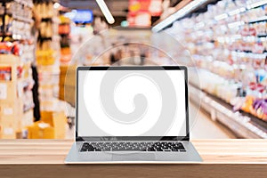 Empty screen laptop on a wooden table with abstract blurred image of supermarket store