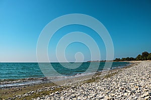 Empty sea shore with white pebble, Landscape sand and round sones on the shore, trees far away, sea and blue sky. Travel. photo