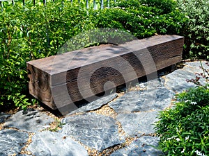Empty seat made from a wooden big log in rectangular shape placed on the stone ground in the green garden.