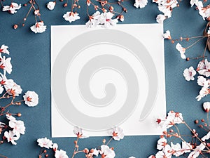 Empty sheet of paper surrounded by small white flowers. Blank card on blue background photo