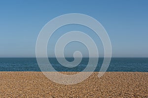 Empty shingle beach with clear blue sky and sea. UK