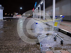 An empty shopping cart in the dark in a store parking lot.