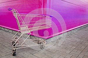 Empty shopping cart parking on violet or pink background with copyspace. retail store.