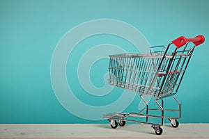 Empty shopping cart on wooden table with green backround. Consumerism concept. Online shopping concept.