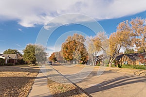 Empty sidewalk and quite neighborhood street with row of suburban house and colorful fall foliage in Texas, USA