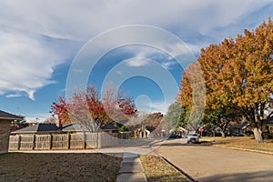 Empty sidewalk and quite neighborhood street with row of suburban house and colorful fall foliage in Texas, USA