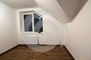 Empty small room with wooden oak parquet floor, newly painted white walls, heating radiator and a window. Attic room