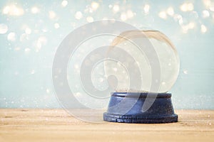 Empty Snow Globe over wooden table with glitter overlay. Magical Christmas concept. Copy space.