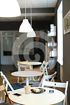 Empty snugly cafe with cups of coffe, smartphones and cake on table.