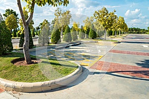 Empty space in city park outdoor concrete parking lot area with blue sky in summer season. Green nature gardening in car parking