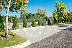 Empty space in city park outdoor concrete parking lot area with blue sky in summer season. Green nature gardening in car parking