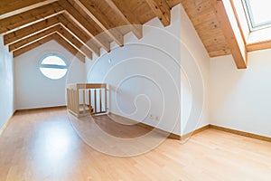 Empty spacious and bright attic in a refurbished apartment with wooden parquet floor and white walls and wooden gable roof