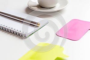 Empty spiral notepad, silver pen, yellow and pink sticker and cup of coffee on white background. Business or education concept