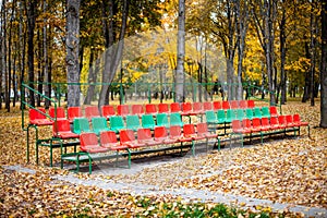 Empty sports grandstand in the leaves in the fall. Yellow leaves lie on a seat of a tribune.