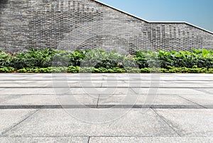 Empty square floor and modern stone wall with green plant in the park