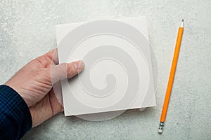 An empty square piece of paper in a man`s hand, a yellow pencil next to it. Mock-up