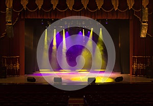 An empty stage of the theater, lit by spotlights and smoke