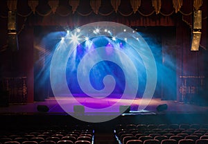 An empty stage of the theater, lit by spotlights and smoke