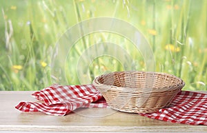 Empty straw basket decorated with checkered kitchen towel on table with green natural background.Easter display