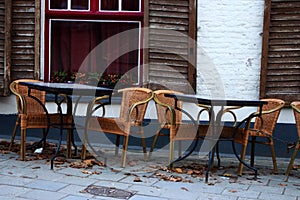 Empty street cafe in european old town. Empty tables and chairs against old white brick building with open shutters and red window