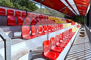 Empty street seats of hippodrome in red and yellow on the podium under a canopy to watch sporting events