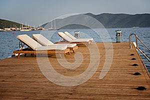 Empty sun beds deck chairs with mattresses on a wooden pier overlooking the blue Mediterranean Sea