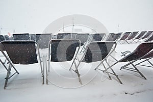 Empty sun lounger chairs out on a terrace during a Winter whiteout blizzard , Les Sybelles, France photo
