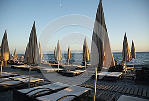 Empty sun loungers and covered beach umbrellas on an evening pebble beach in Sochi