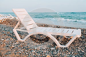 Empty Sun loungers in front of sea. Sun chairs on sandy beach. Big waves stormy weather. An empty chaise longue and