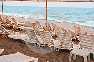 Empty Sun loungers in front of sea. Sun chairs on sandy beach. Big waves stormy weather. An empty chaise longue and