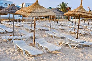 Empty sun loungers without people under straw umbrellas on the beach
