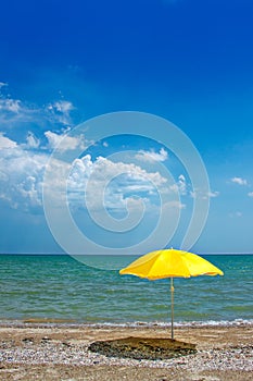 An empty sunny sandy sea beach with a yellow umbrella