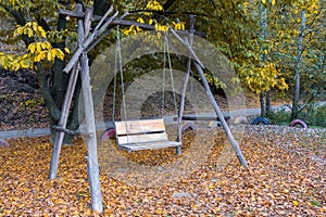 Empty swing in an autumn park, a wooden swing hanging on a chain and made by hand, against a background of yellowed autumn foliage