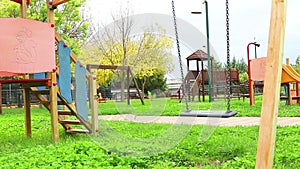 Empty swing with chains swaying at playground for child, moved from wind, on green meadow background
