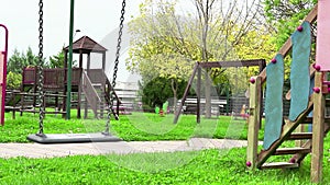 Empty swing with chains swaying at playground for child, moved from wind, on green meadow background in slow motion loopable