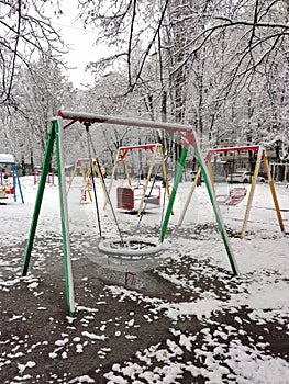 Empty swing in kindergarten in snow and mud