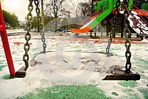 Empty swing in a park covered with melting snow