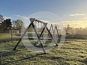 Empty swings in a children's playground in early morning haze.