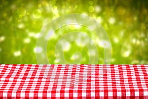 Empty table background. Empty wooden deck table covered with a red checkered tablecloth in front of abstract blurred fresh