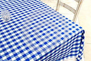 Empty table covered with blue and white chequered tablecloth next to white wooden chair.