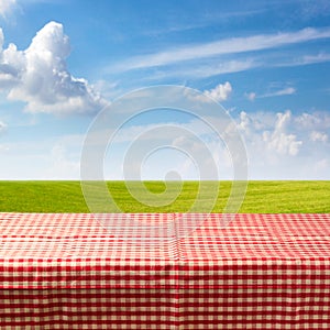 Empty table covered with checked tablecloth over green meadow and blue sky photo