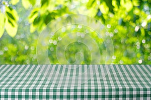 Empty table with green tablecloth over blur garden and bokeh background