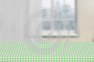Empty table product. Empty wooden deck table covered with a green white checkered tablecloth against blurred curtains background.