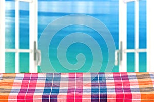 Empty table product. Empty wooden table covered with a colorful checkered tablecloth over abstract blurred ocean background. Space