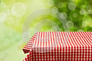 Empty table with red checked tablecloth over green bokeh background. photo