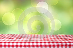 Empty table with red checkered tablecloth and bright green bokeh background. For your food and product display montage.