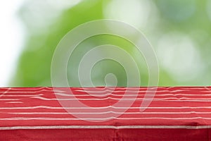 An empty table with a red striped tablecloth and an green natural background in the morning in the garden. For your food and prod