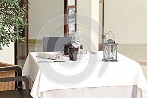 An empty table for two in a restaurant, covered with a white tablecloth with two table sets and a lantern, in a cafe or restaurant